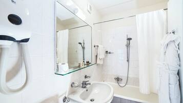 Un baño moderno con un lavabo con estructura de vidrio, un cabezal de ducha de mano y una bañera.