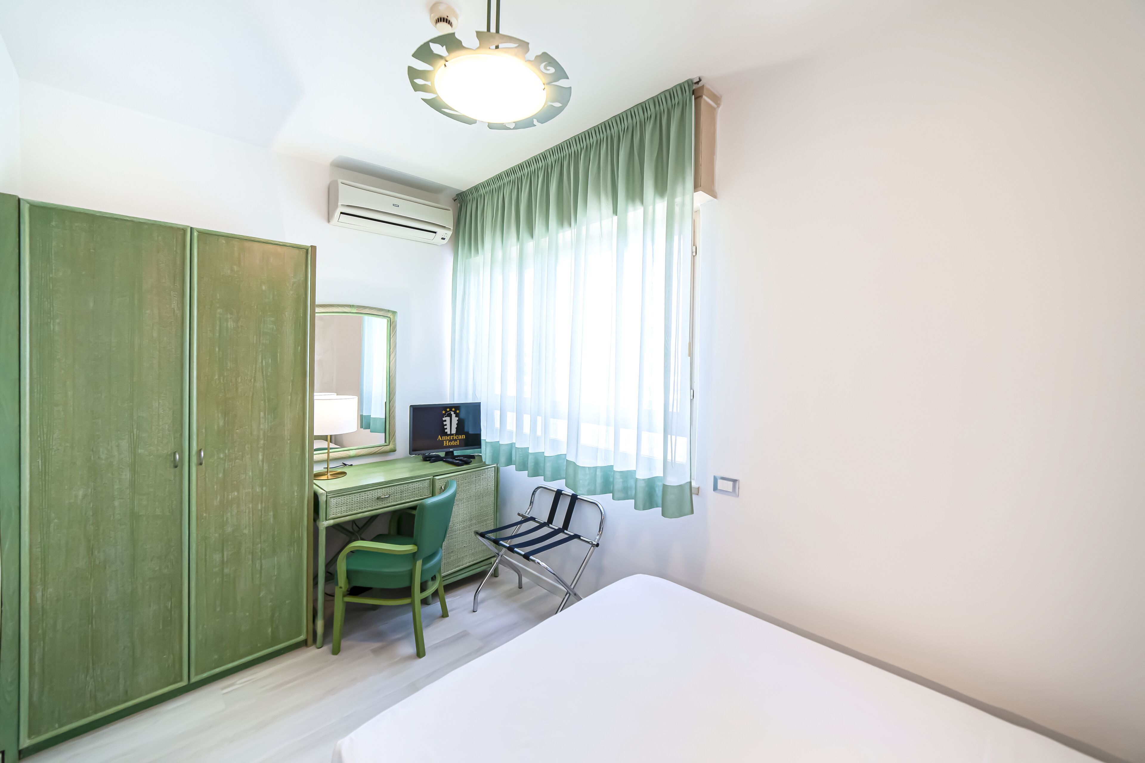 A room with a bed, a desk with a chair, a television, and a wardrobe.