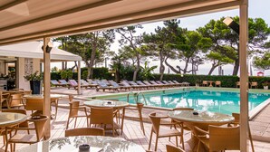 Ett område vid poolen med solstolar och bord, en pool och utsikt över havet.