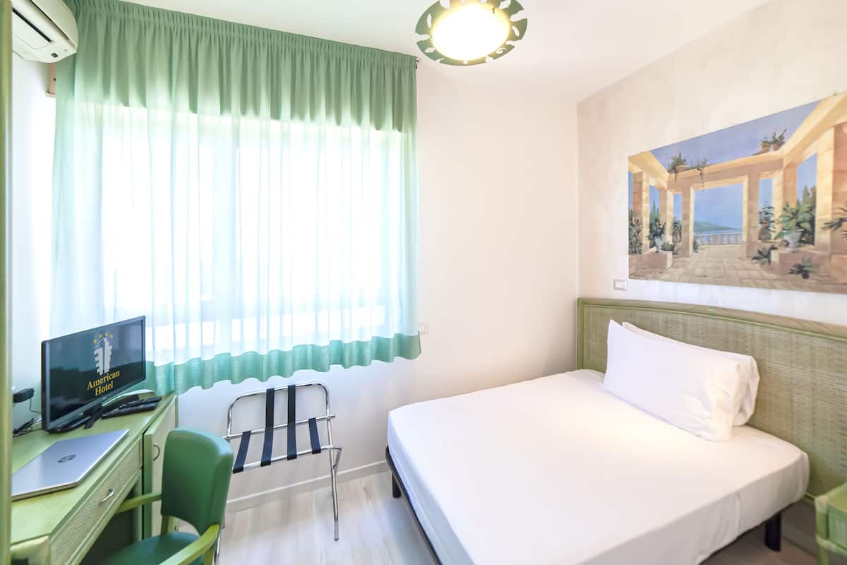Ein Hotelzimmer mit Bett, Schreibtisch mit Computer, Stuhl und einem Bild an der Wand.