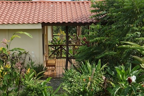 Une petite maison avec un toit en tuiles et une terrasse en bois, entourée d’une végétation luxuriante.