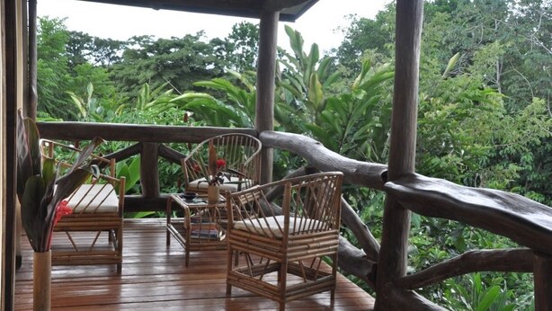 A wooden deck with wicker furniture and a view of lush greenery. - Rancho Las Tilapias (Parrita)