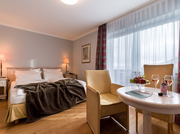 Habitación de hotel con cama, una silla, una mesa con frutera y una botella de vino.