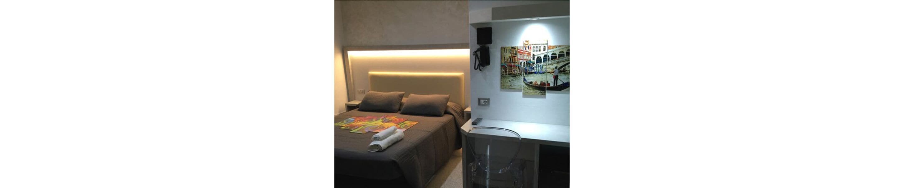 A hotel room with a bed, a nightstand, a lamp, and a wall-mounted painting.