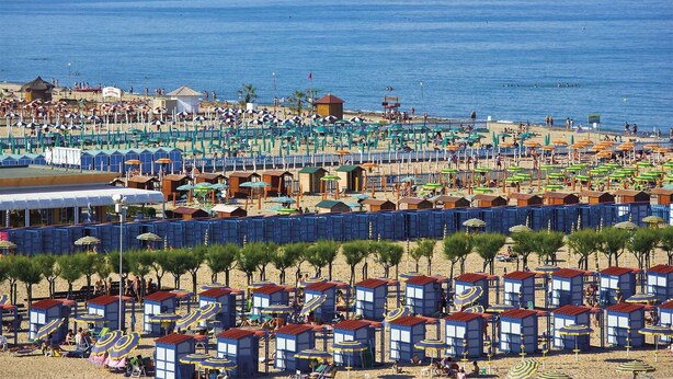 A beach with numerous beach huts and umbrellas, a sandy beach, and a clear view of the sea.