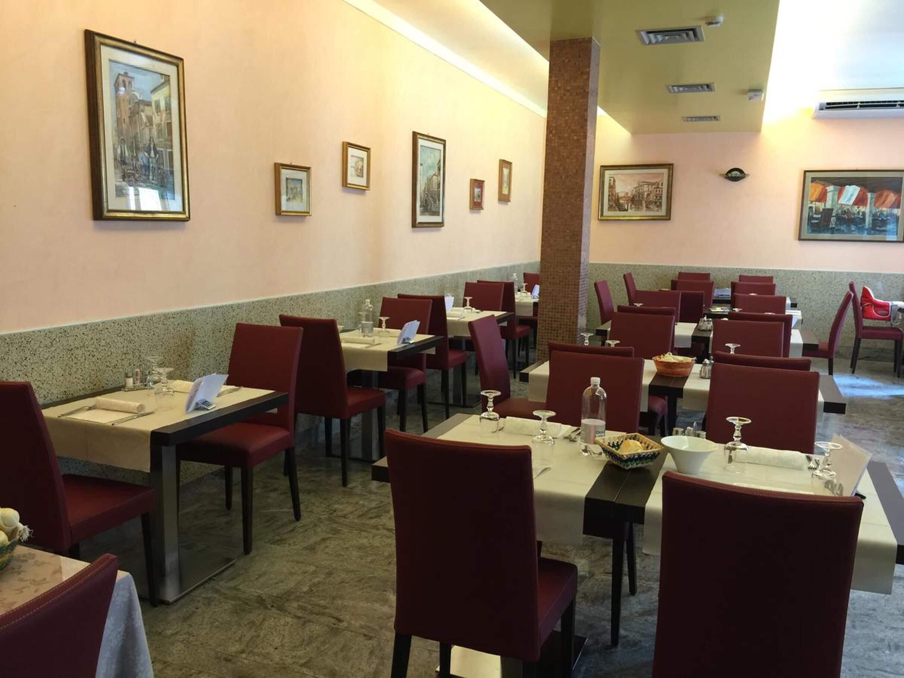 Un restaurant doté de nombreuses tables et chaises, avec des œuvres d’art encadrées accrochées aux murs et un sol carrelé.