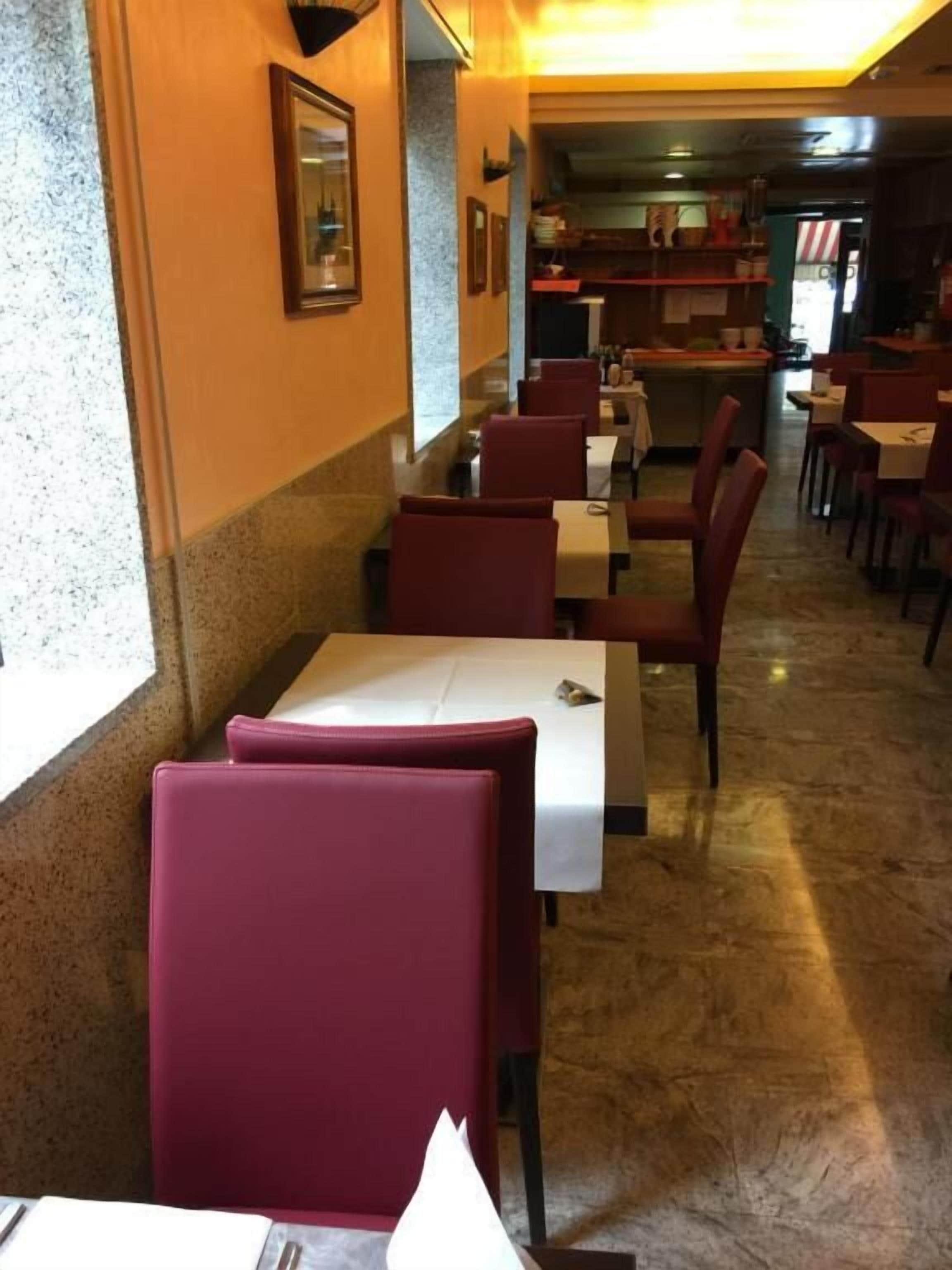 A restaurant interior with marble flooring, red upholstered booths, and a kitchen area in the background.