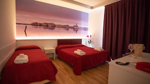 A hotel room with two beds, a desk, a large window with a cityscape view, and a minibar.