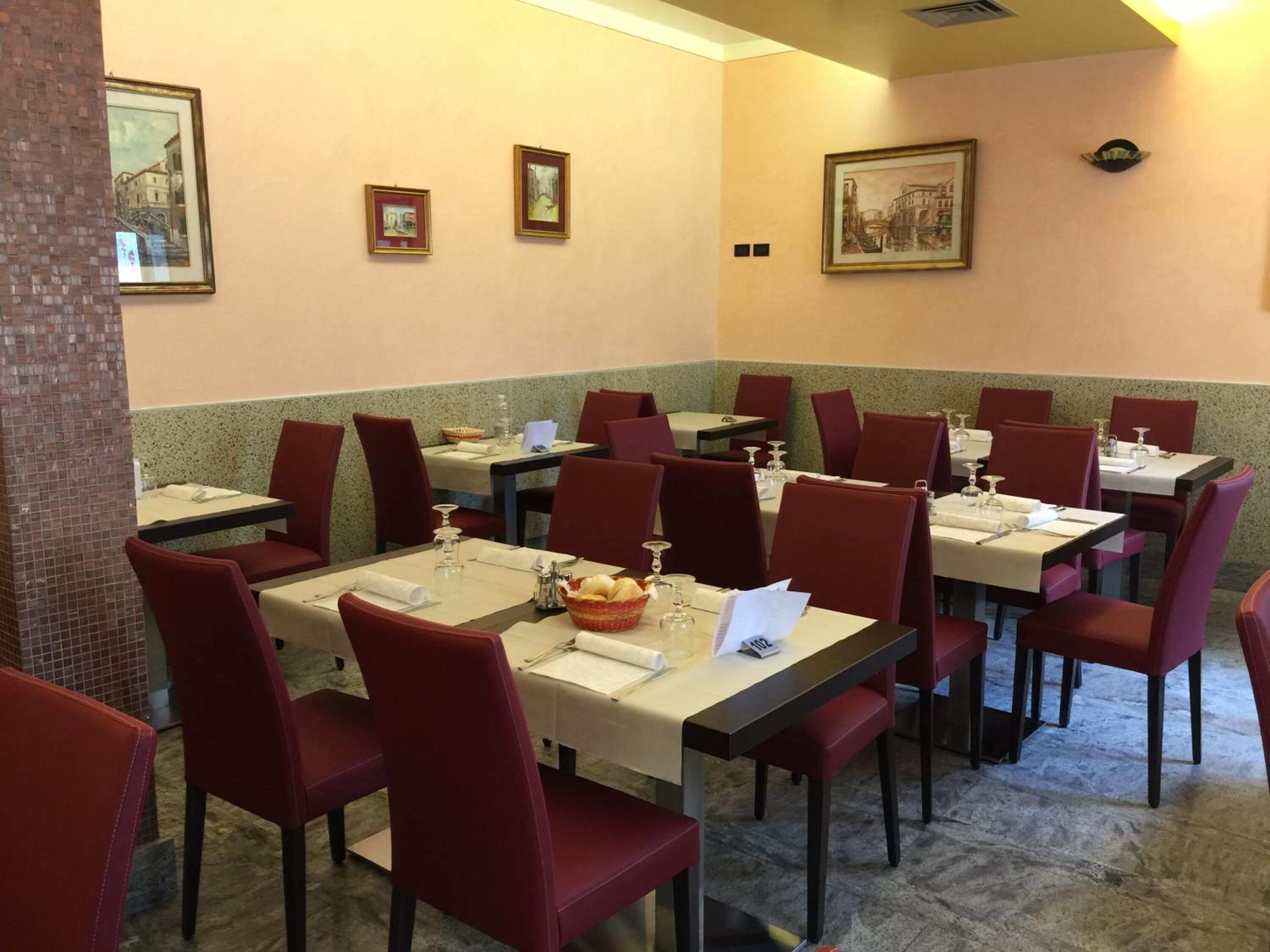 Un restaurant avec des tables dressées, des chaises rouges et des œuvres d’art encadrées accrochées aux murs.