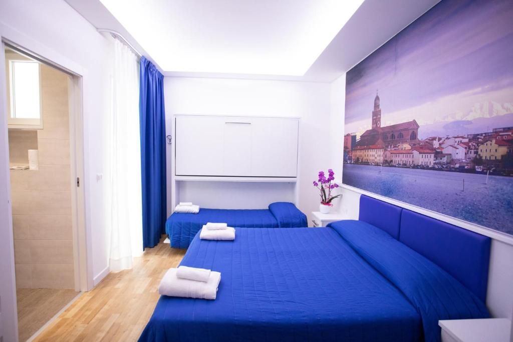 A hotel room with two beds, a large window with a cityscape view, and a door leading to a bathroom.