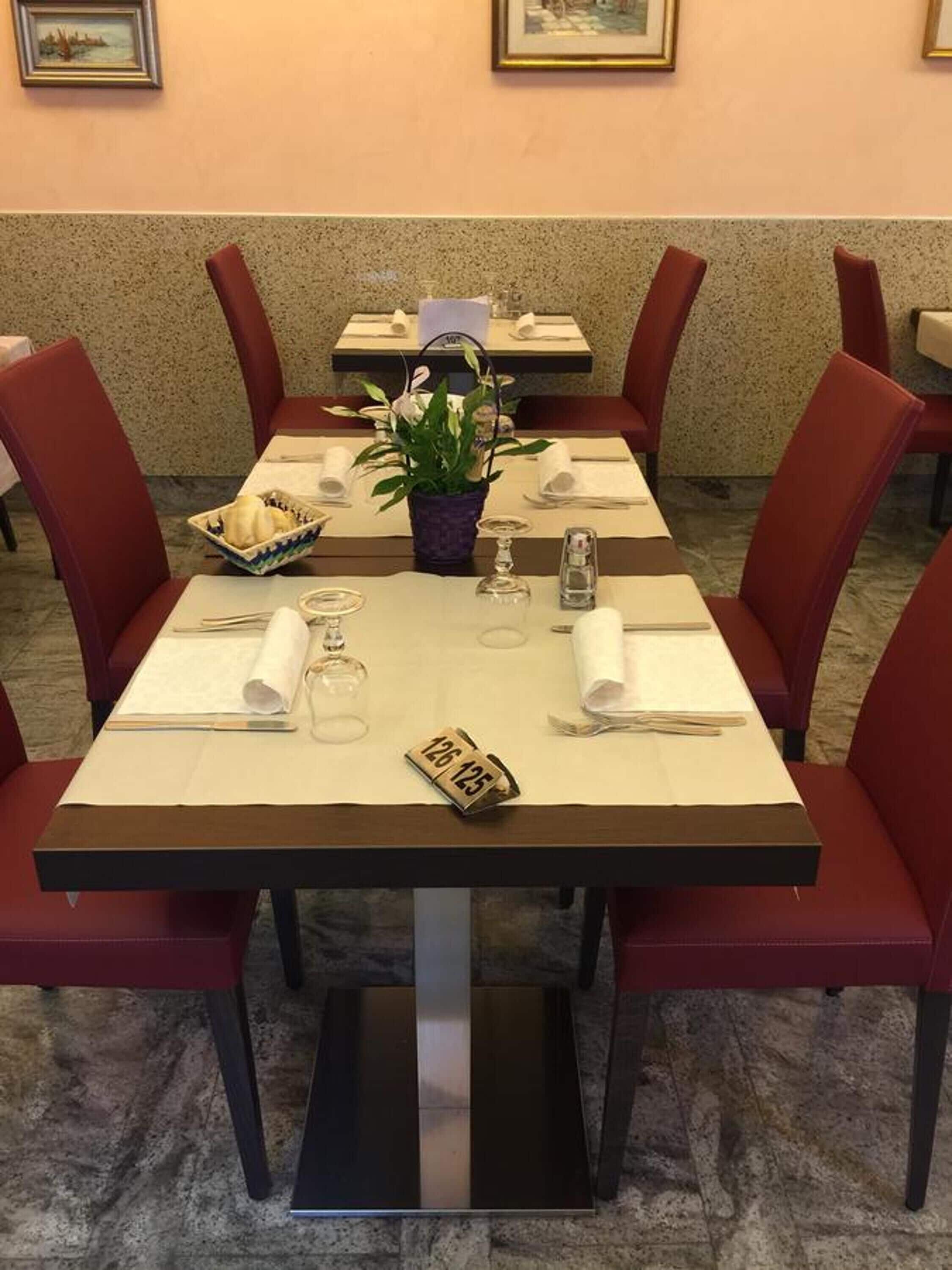 A dining area with tables set for four, each with a white tablecloth, red chairs, and a small potted plant.