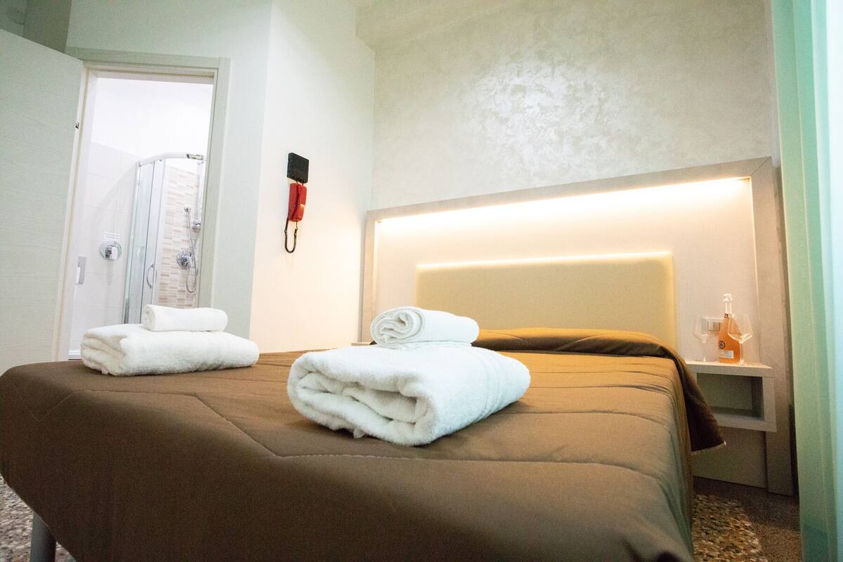 Une chambre d’hôtel comprenant un lit, une table de chevet, un téléphone et un espace douche.