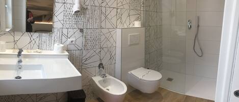 A modern bathroom with a white sink, bidet, and toilet, a mirror, and a shower with a handheld showerhead.