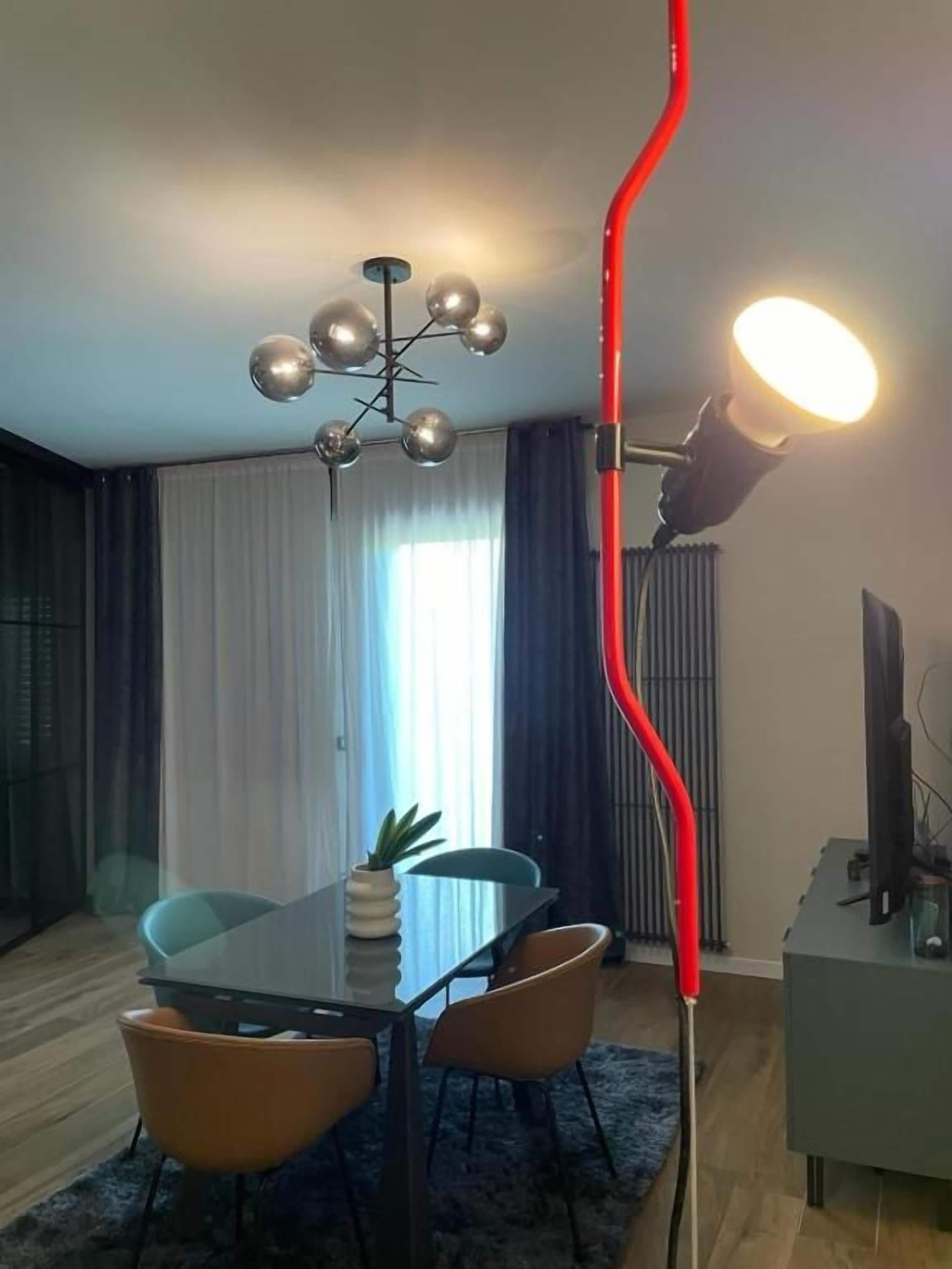 A modern dining area with a glass table, chairs, a chandelier, and a red light fixture.