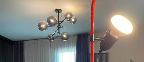 A modern dining area with a glass table, chairs, a chandelier, and a red light fixture.