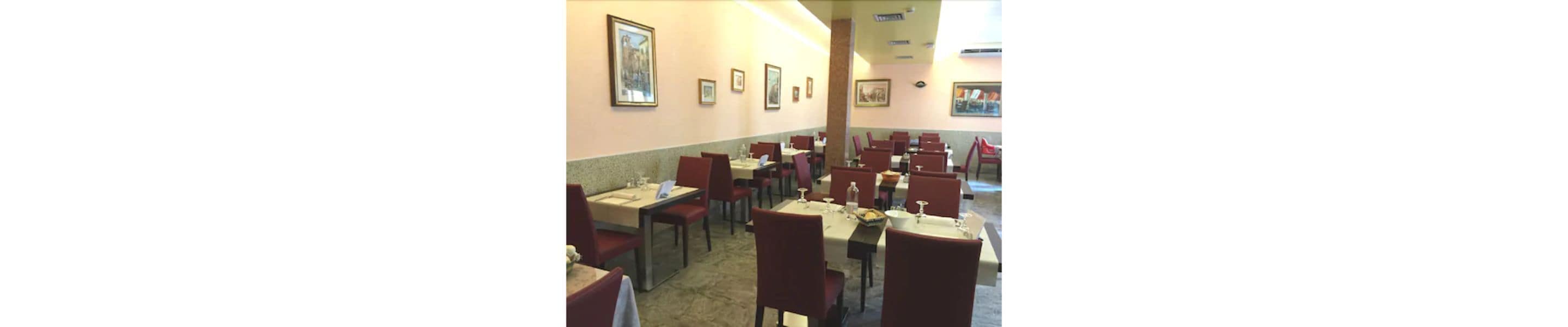 En restaurant med flere borde og stole, billeder på væggen og et tæppe på gulvet.