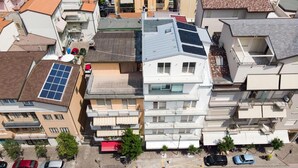 An aerial view of a residential area with multiple buildings, including a prominent white building with balconies and solar panels on the roof.