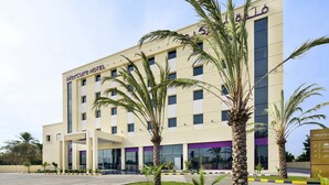 A hotel with a modern facade, palm trees in the foreground, and a clear sky.