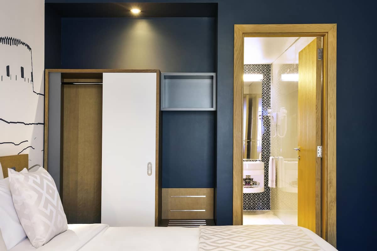 A hotel room with a bed, a wardrobe, a mirror, and a bathroom visible through an open door.