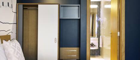 A hotel room with a bed, a wardrobe, a mirror, and a bathroom visible through an open door.