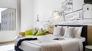 A hotel room with a bed, a green armchair, a nightstand, and a wall mural. - Mercure Sohar (Sohar)