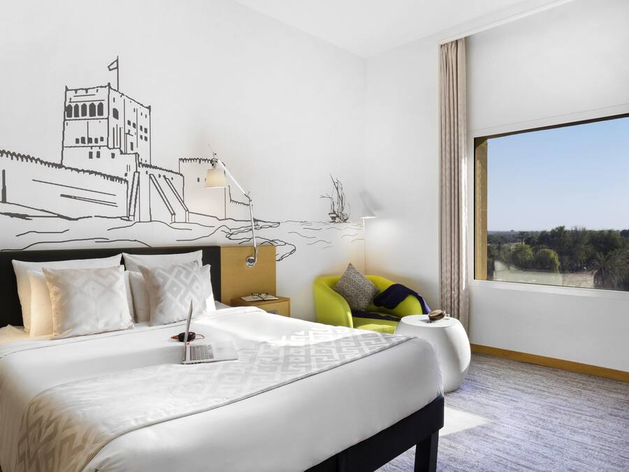 Une chambre d’hôtel avec un grand lit, une table de chevet, une lampe et une vue sur l’extérieur.