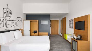 Quarto de hotel com cama, guarda-roupa, secretária com chaleira, televisão e parede com um mural de paisagem urbana.