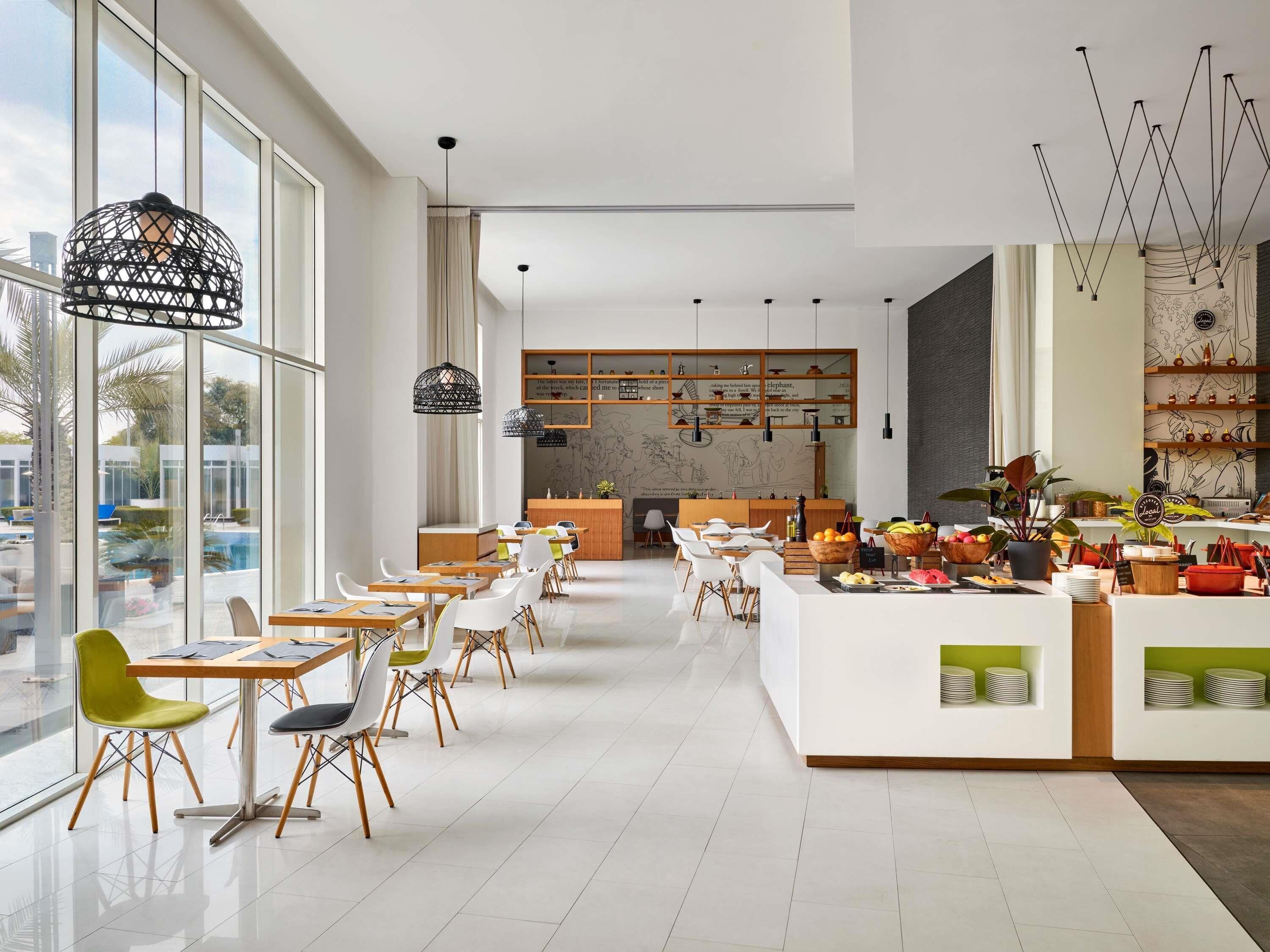 Un restaurante moderno con una barra larga, sillas blancas y vistas a una piscina.