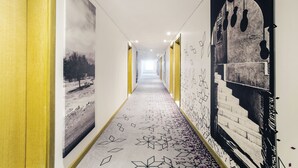 A hallway with a patterned carpet, yellow walls, and artwork on the walls.