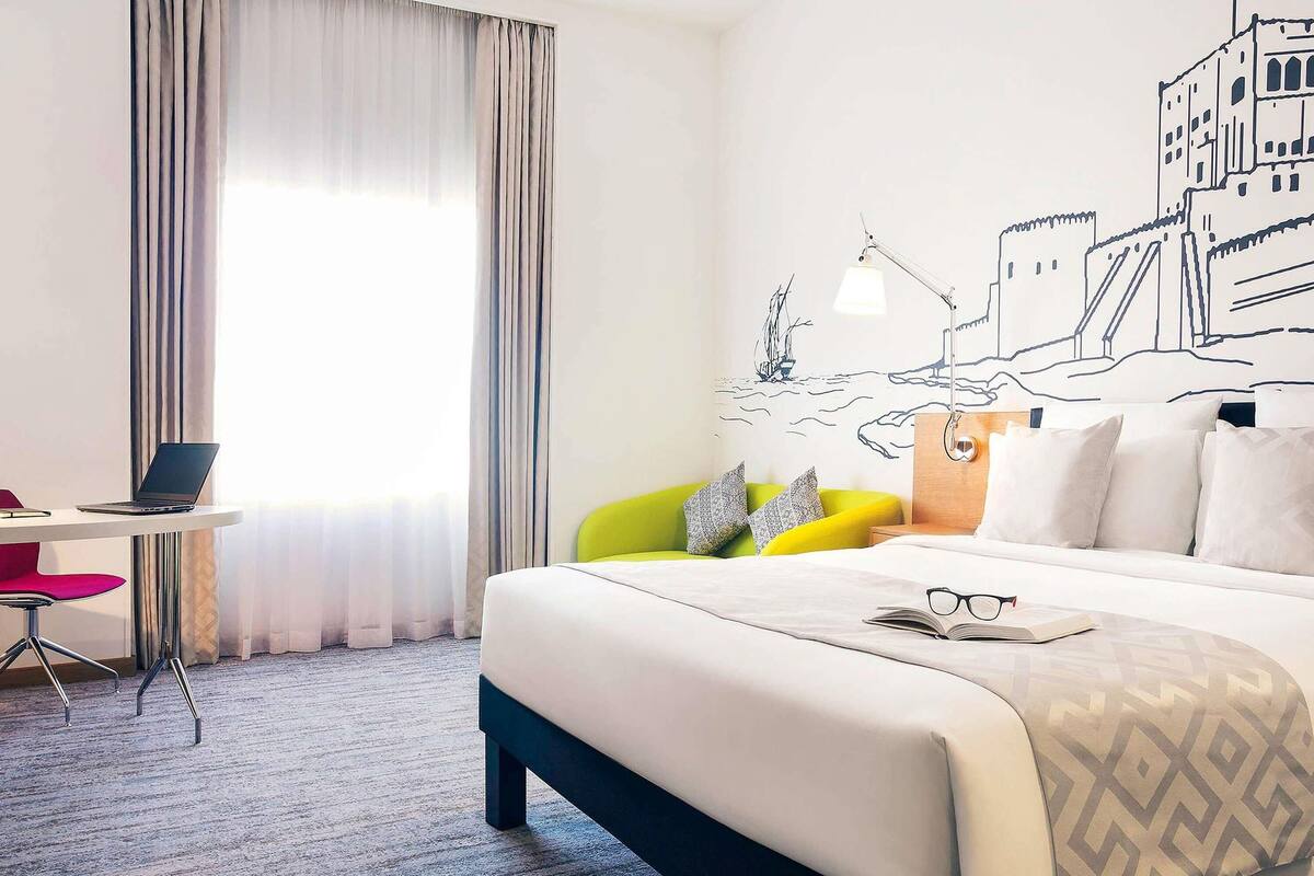 Una camera d'albergo con un letto, una scrivania con un portatile, una sedia e un murale.