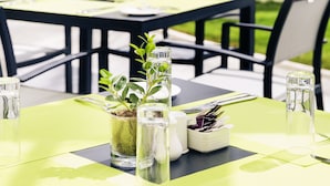 An outdoor dining area with tables set for two, featuring green placemats and clear glassware.