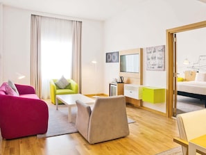 A modern hotel room with a wooden floor, a bed, a desk, a chair, a sofa, and a TV. - Mercure Sohar (Sohar)