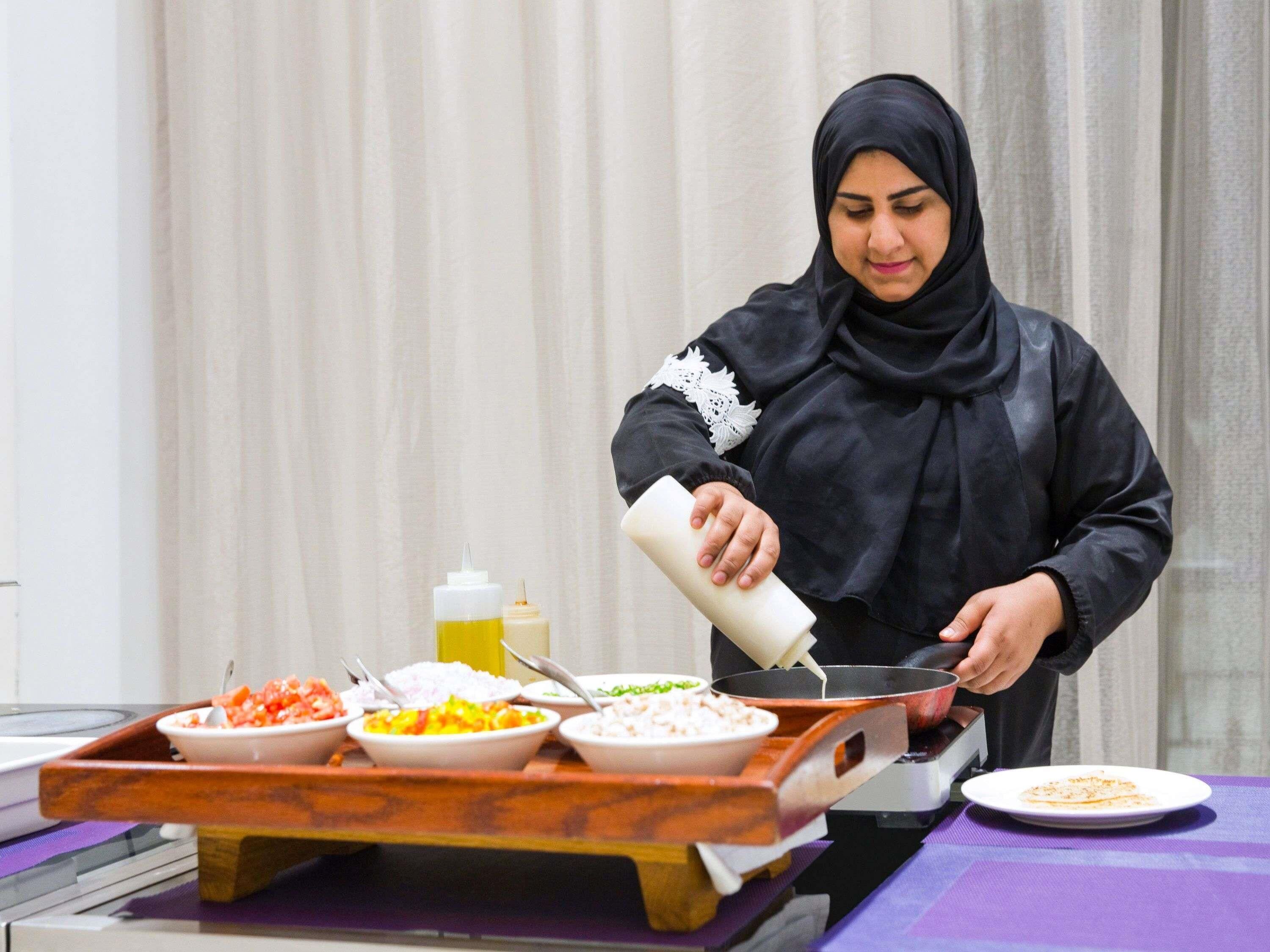 A person pouring sauce into a pan on a tray with various dishes.