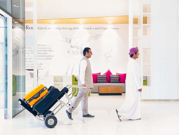 A modern hotel lobby with a minimalist design, a luggage cart, and a seating area with colorful cushions. - Mercure Sohar (Sohar)