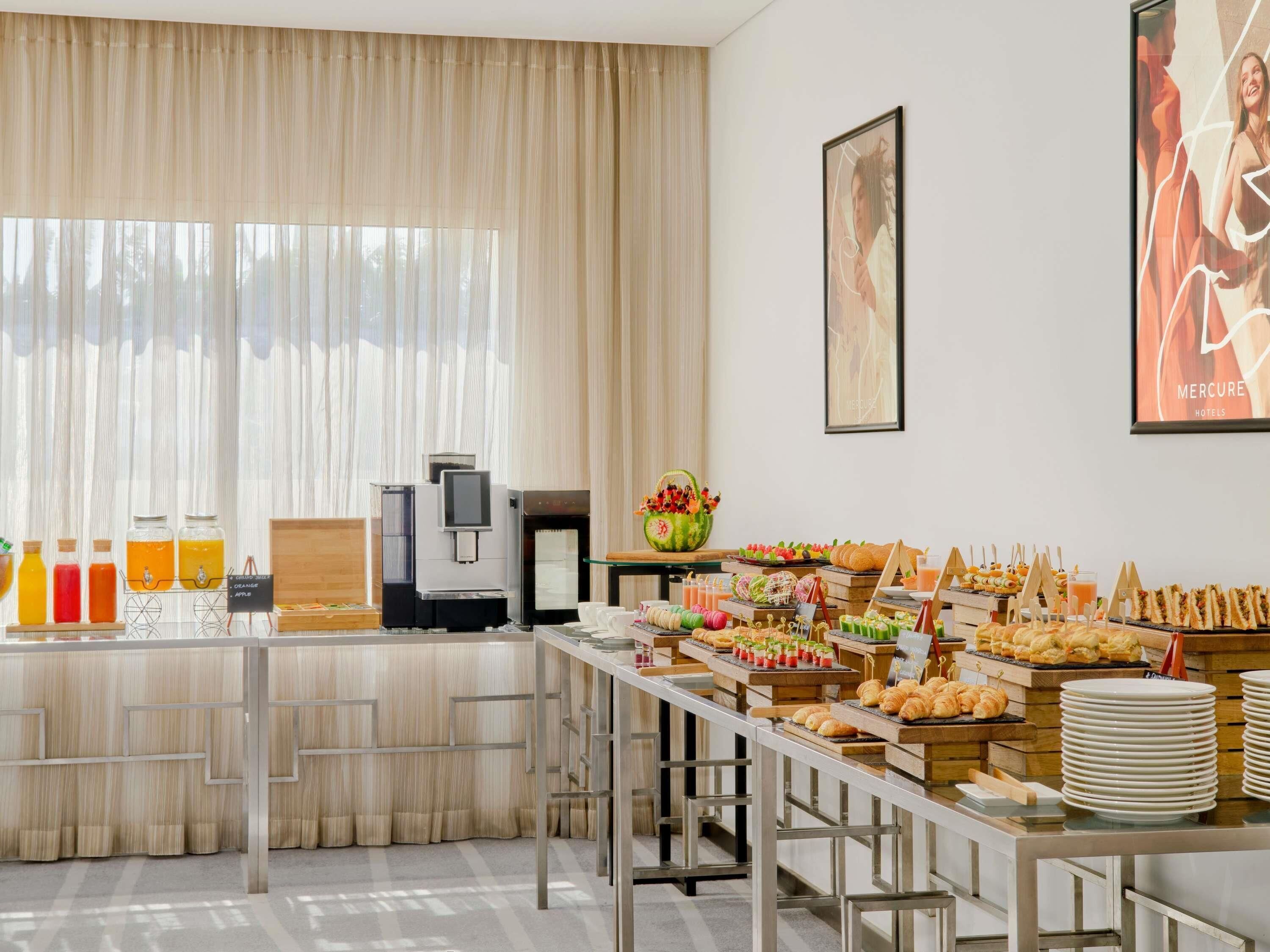 A breakfast buffet with various food items, a coffee machine, and a large window with curtains.