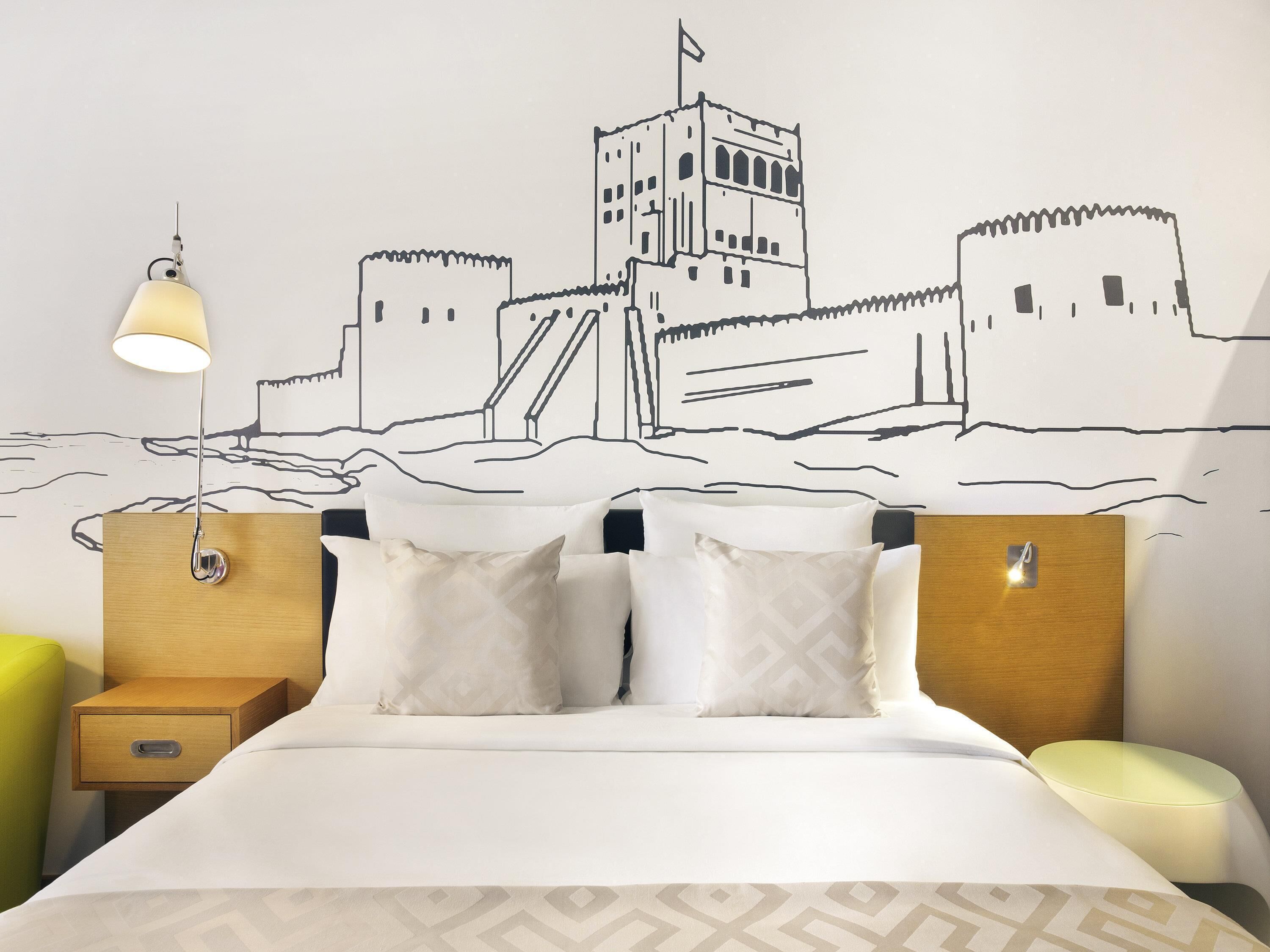 A hotel room with a bed, two bedside tables, a nightstand, and a wall mural.