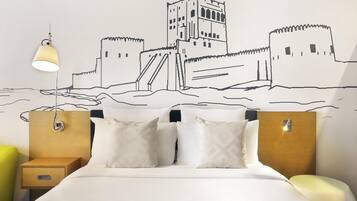 A hotel room with a bed, two bedside tables, a nightstand, and a wall mural.