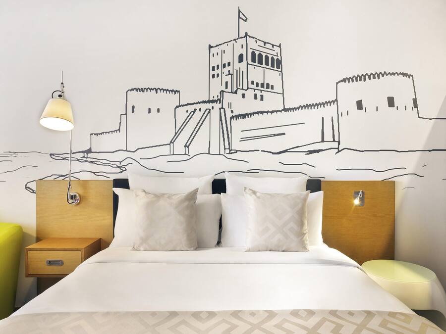 A hotel room with a bed, two bedside tables, a nightstand, and a wall mural.