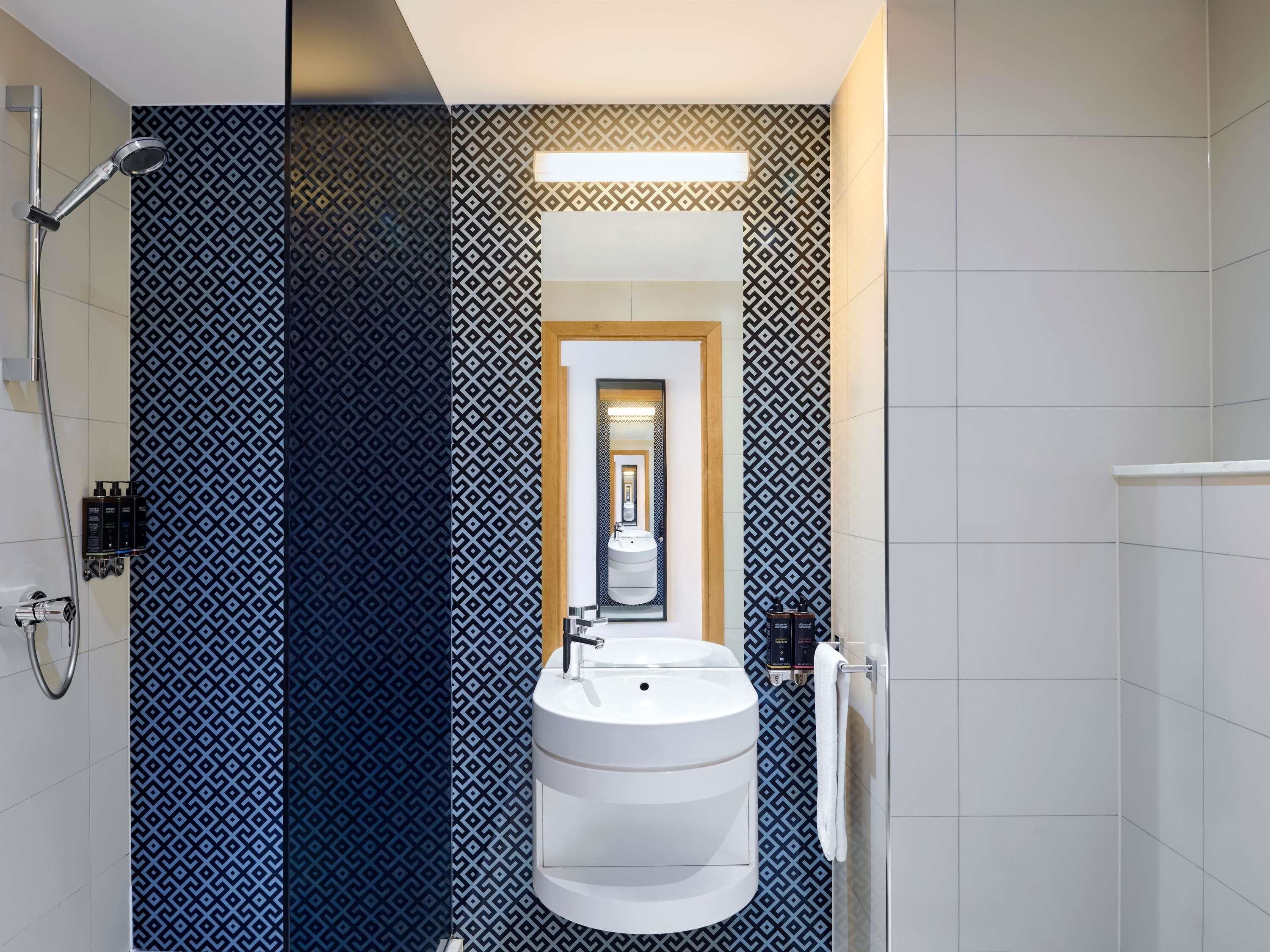 A modern bathroom with a geometric patterned wall, a white sink, and a shower.