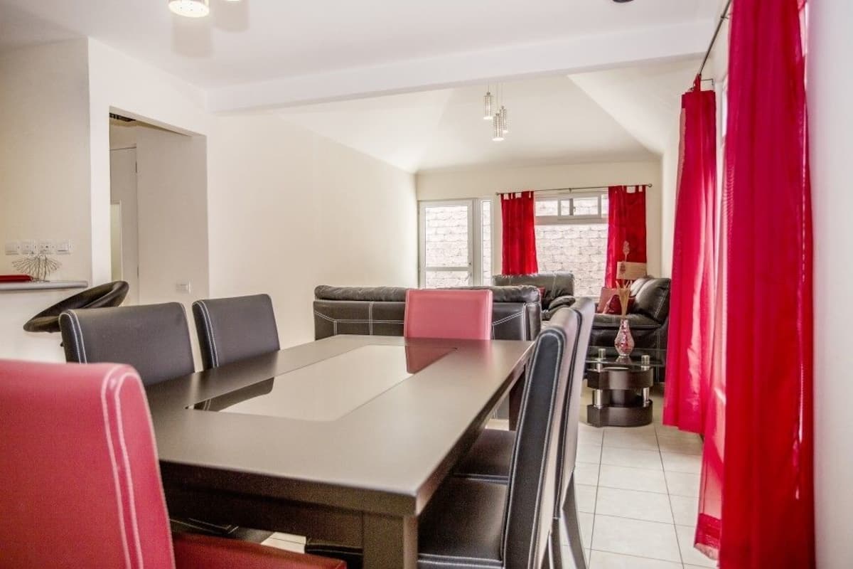A modern dining area with a long table, black and red chairs, and a sofa in the background.