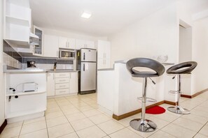 Una cocina moderna con armarios blancos, un microondas, un refrigerador y dos taburetes de bar.