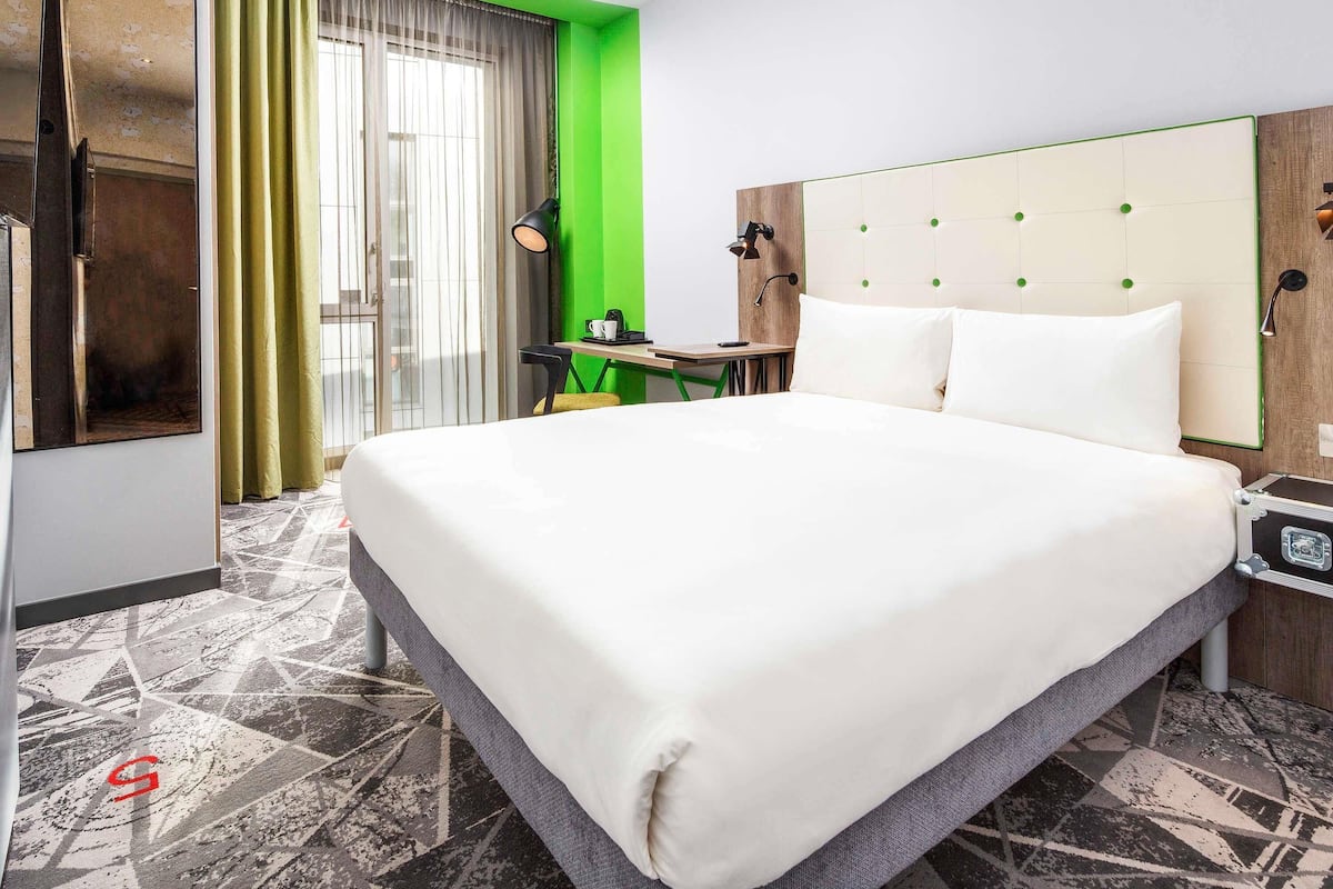 Habitación de hotel con cama, escritorio, silla, máquina de café y maleta.
