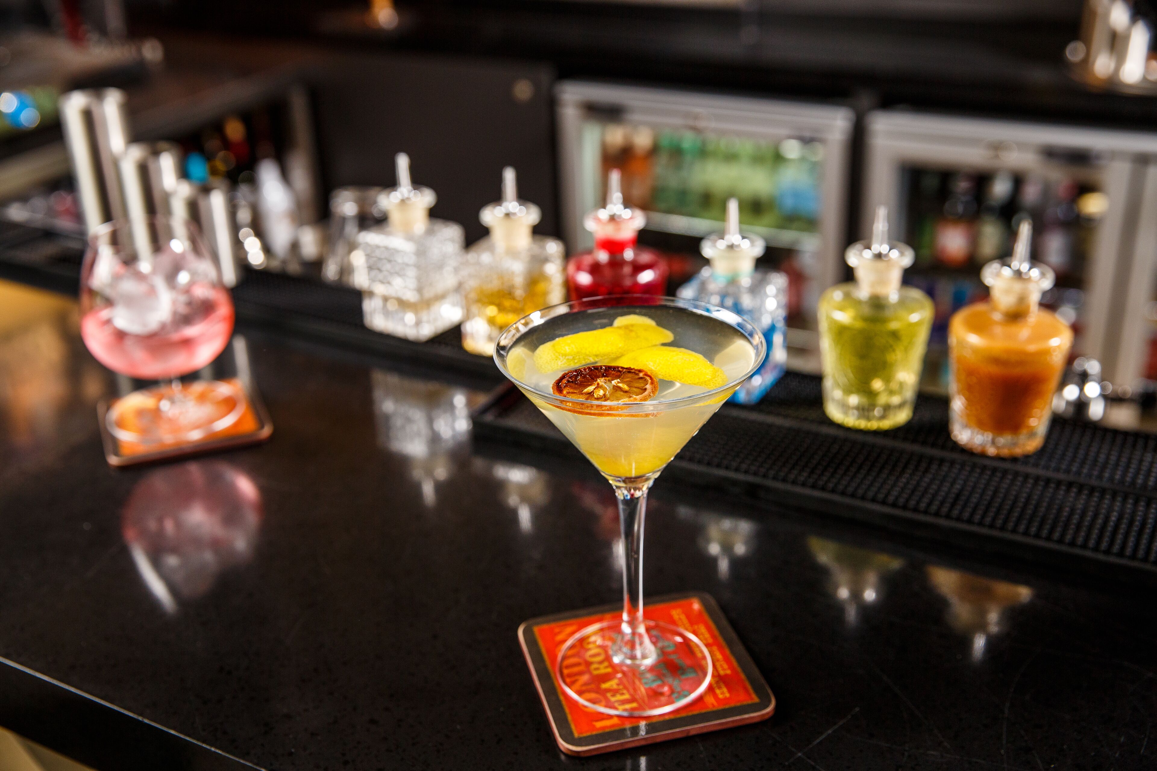 A bar with a martini glass on a coaster, surrounded by various bottles and glasses.