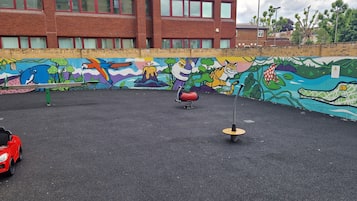 A playground with a colorful mural, a red toy car, and a swing set.