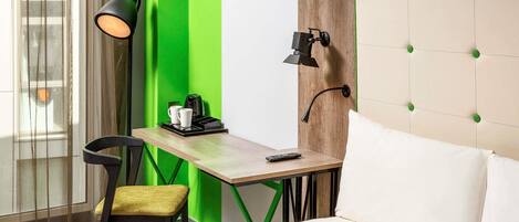 Una camera d'albergo con un letto, una scrivania con una sedia, una lampada e una macchina per il caffè.
