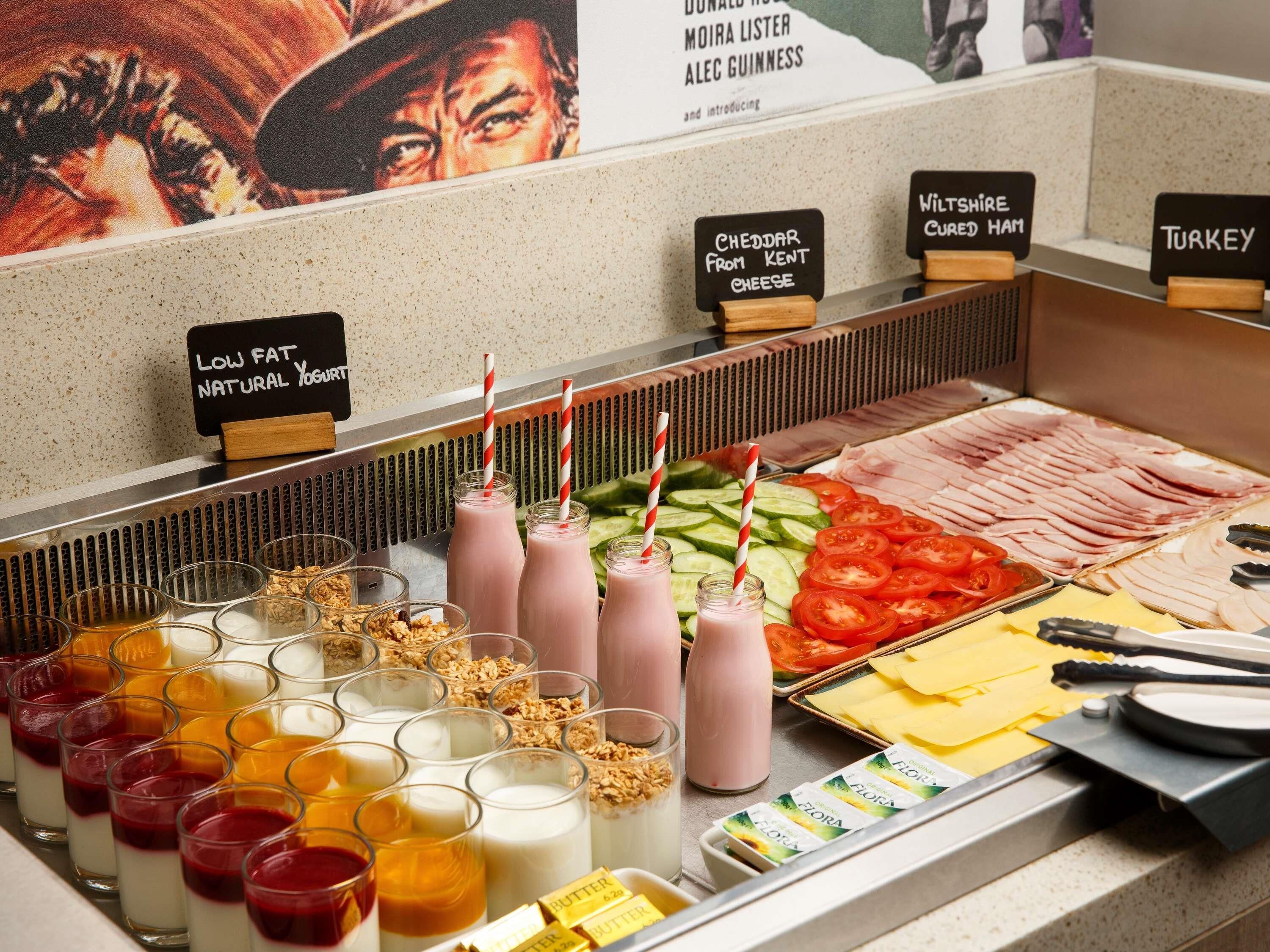 Un bufé con diferentes opciones de comida y bebidas, incluyendo carnes cortadas, quesos y una selección de jugos y batidos.