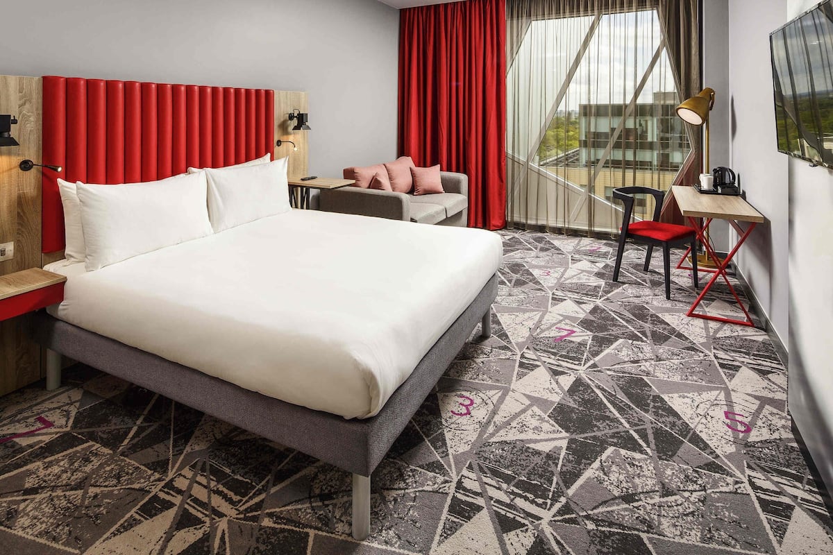 A hotel room with a large bed, a desk, a chair, and a view of the outside.