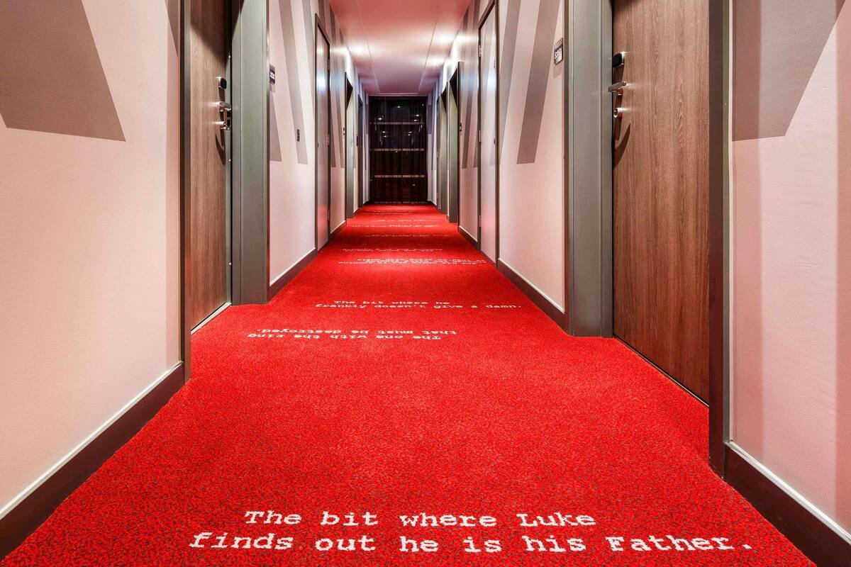 A hotel hallway with red carpet and doors on both sides.