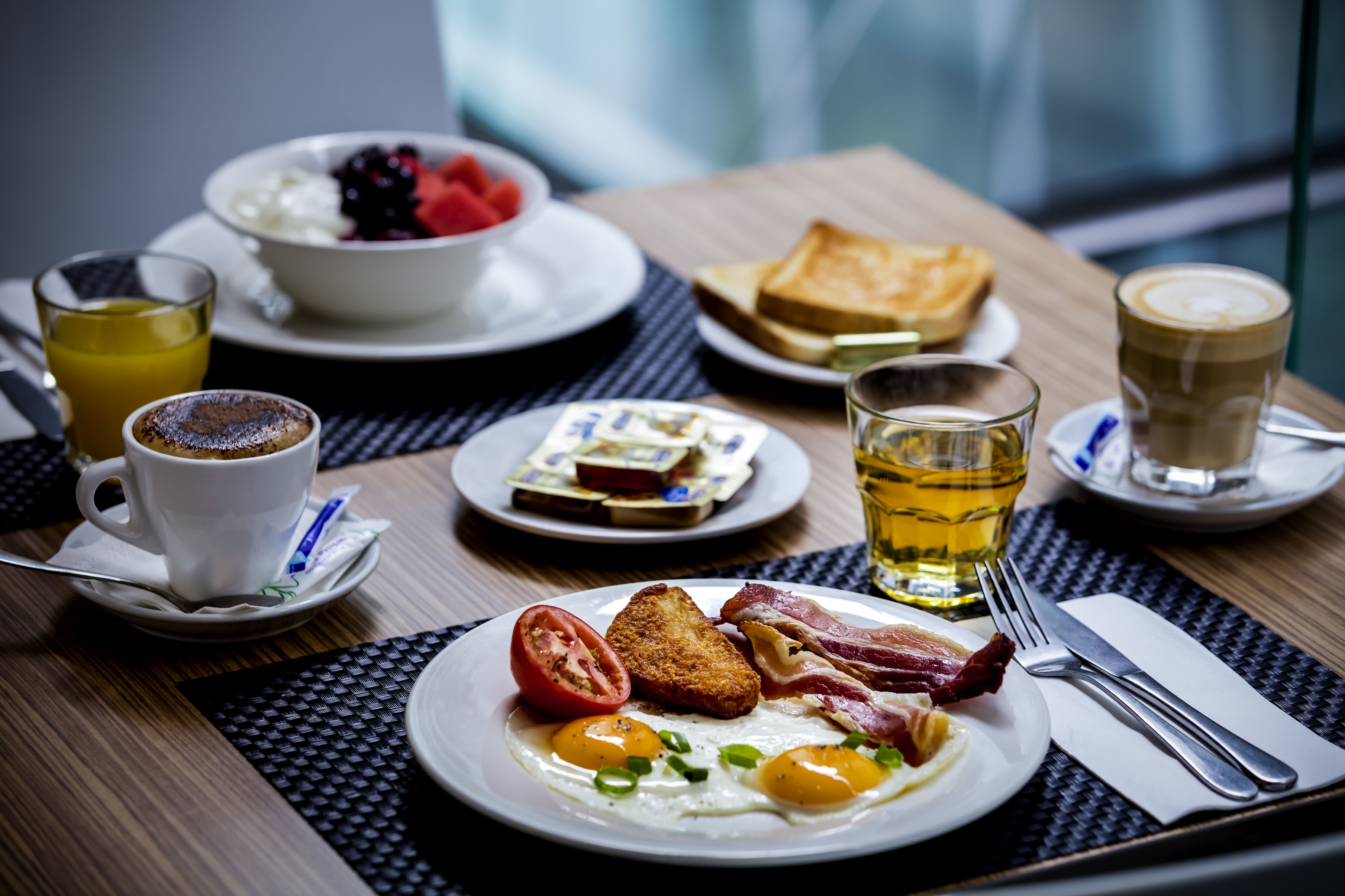 Uma mesa de café da manhã com torradas, ovos, bacon e uma xícara de café.