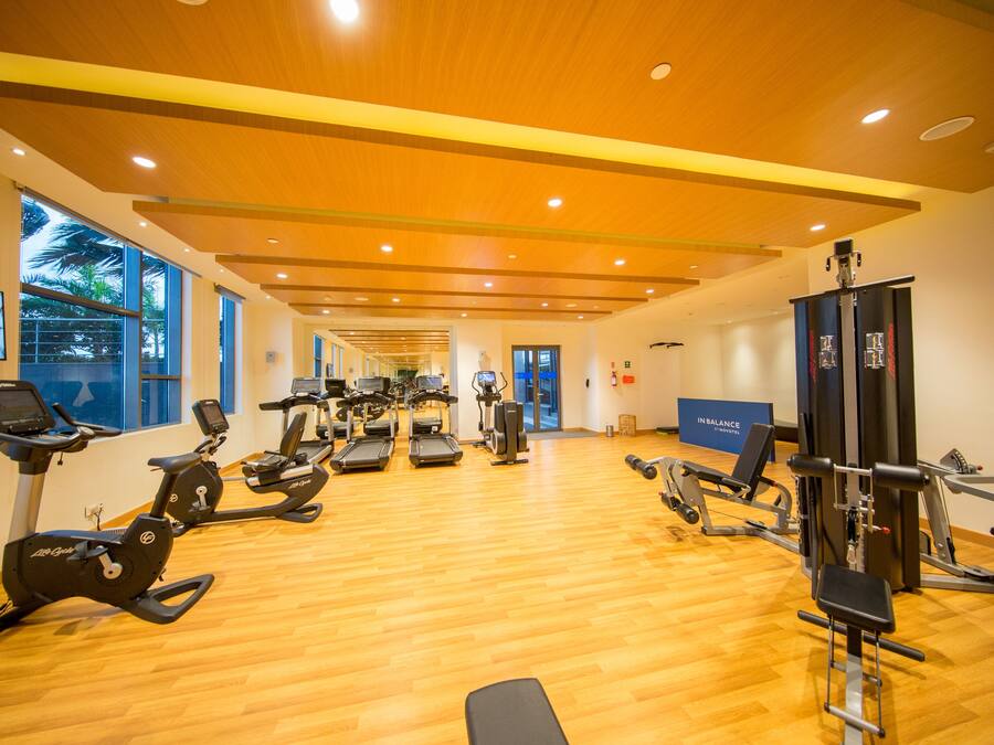 Un gimnasio con máquinas de cardio, equipo de entrenamiento con pesas y un espejo grande.